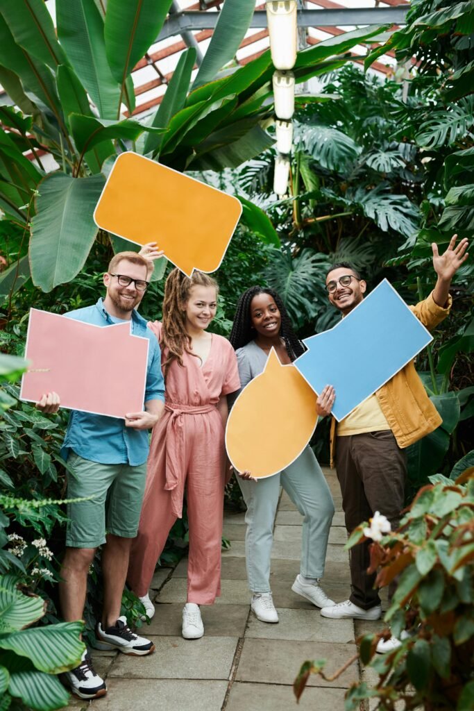 pexels-photo-3228812-3228812 Cheerful group of friends holding colorful speech bubbles in a lush greenhouse setting.