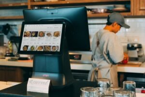 pexels-photo-12935084-12935084 Digital ordering system in a restaurant kitchen with a touchscreen display and a chef at work.